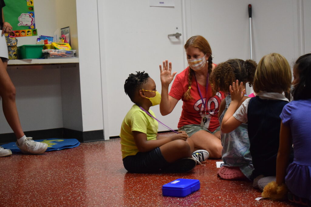 Kelly sits in floor with four young acting students in a classroom with a red floor.